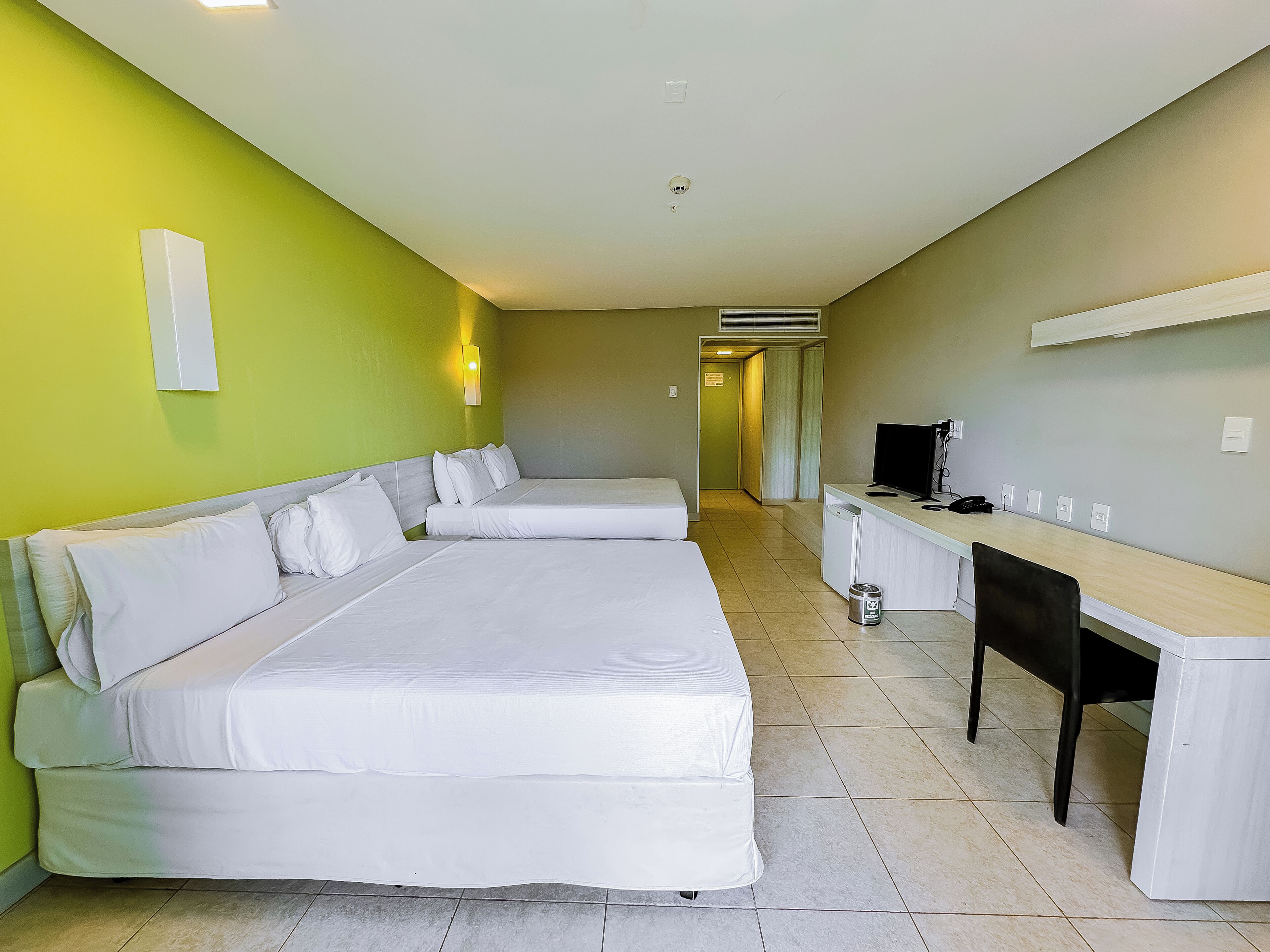 A hotel room with two beds, a desk, a chair, and a television.