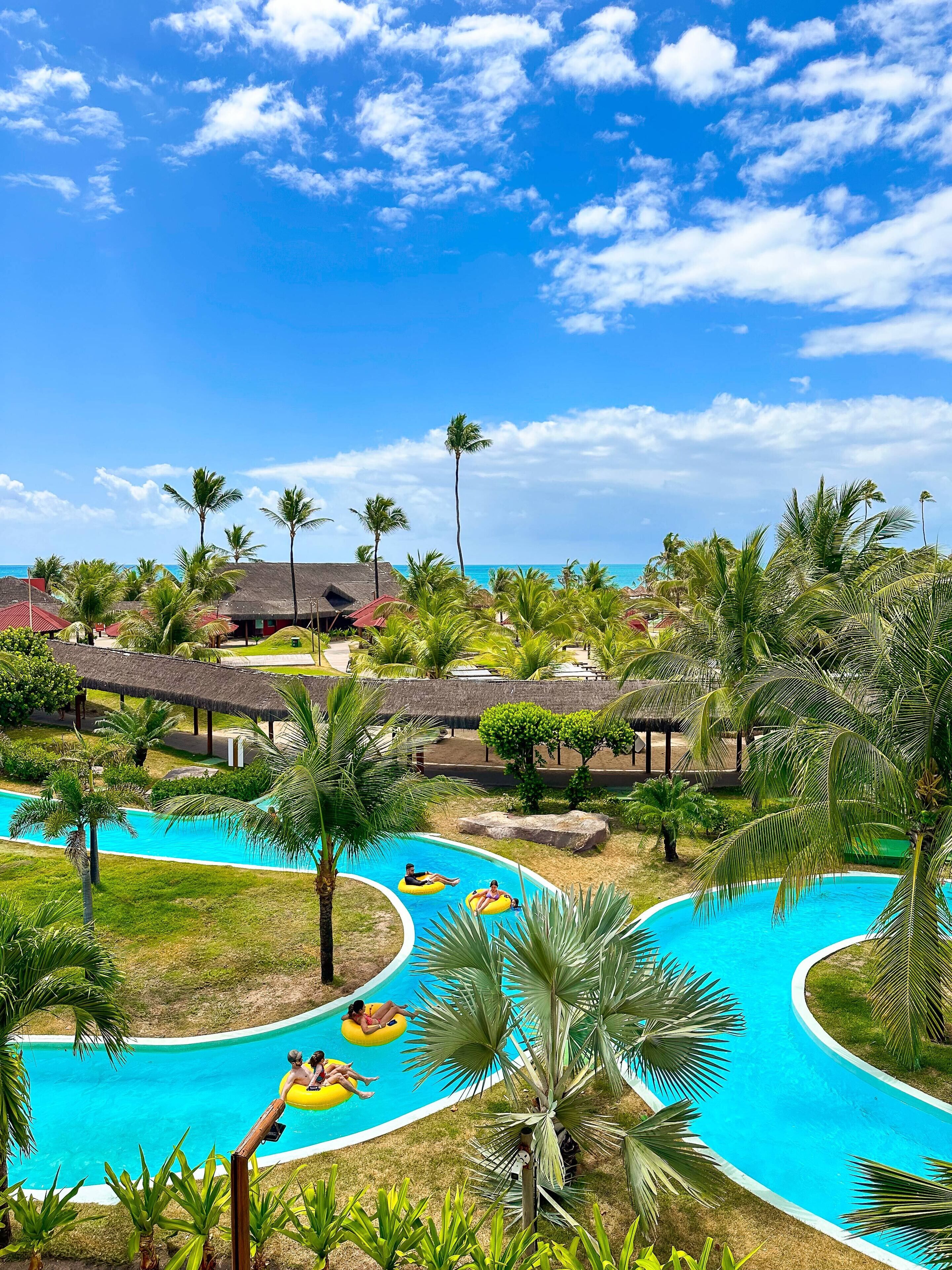 Ein Resort mit Swimmingpool, Palmen und strohgedeckten Hütten.