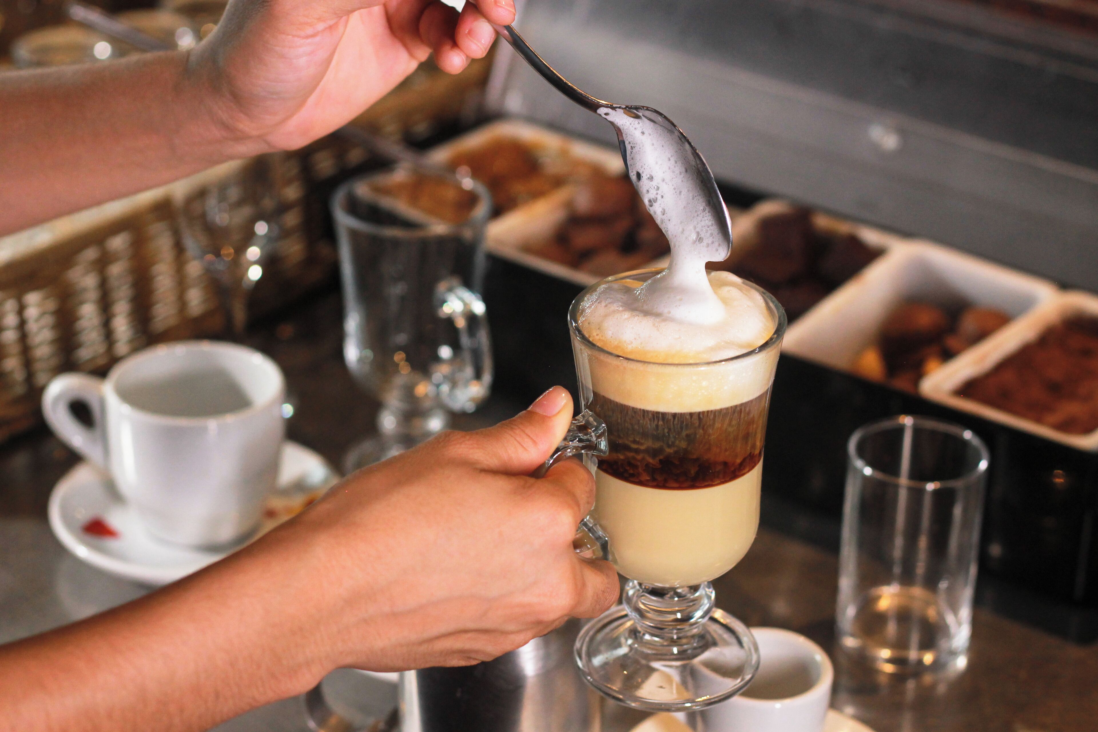 A person stirring a layered beverage in a glass.