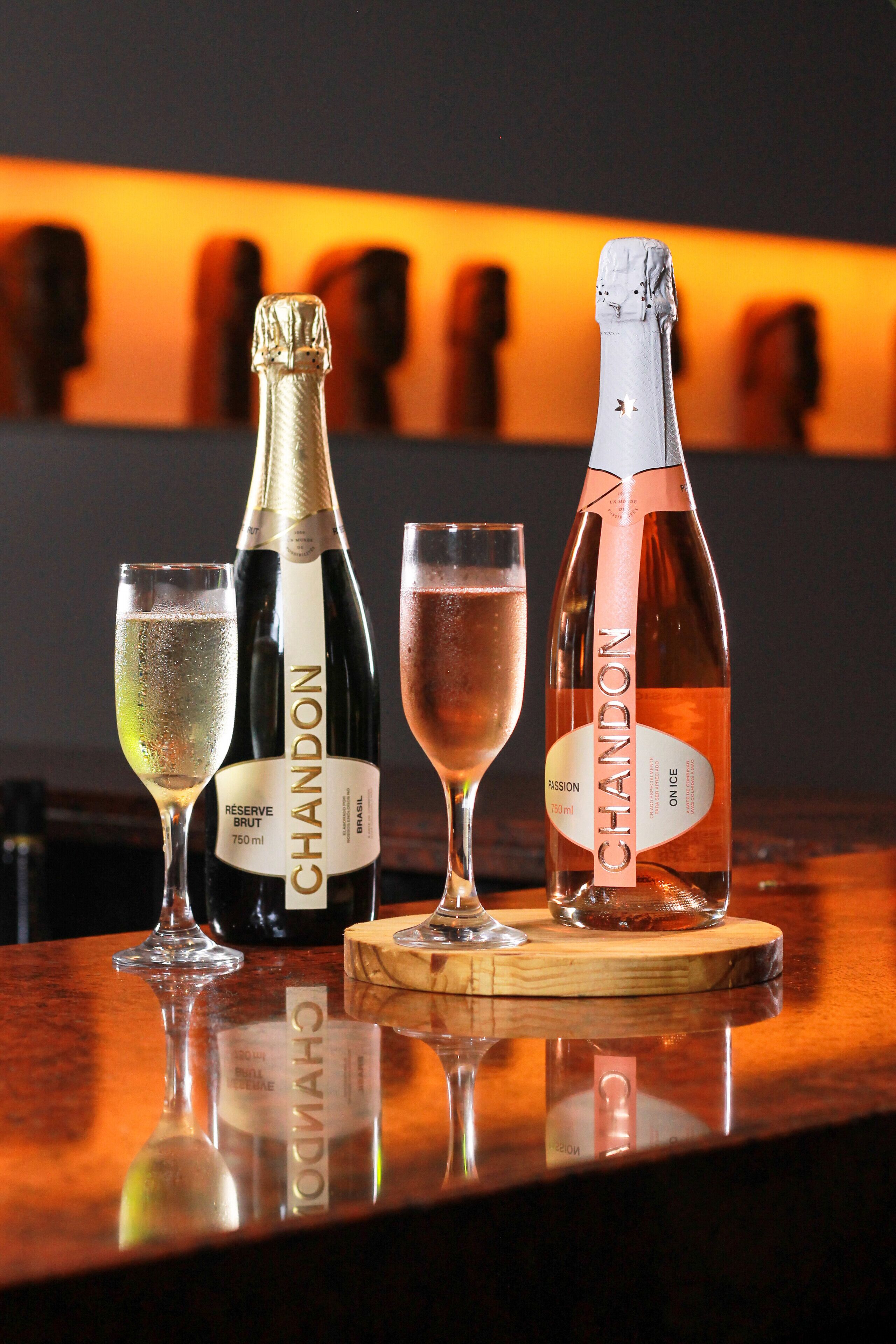 Drei Flaschen Chandon Champagner und zwei Gläser auf einem Holzteller.