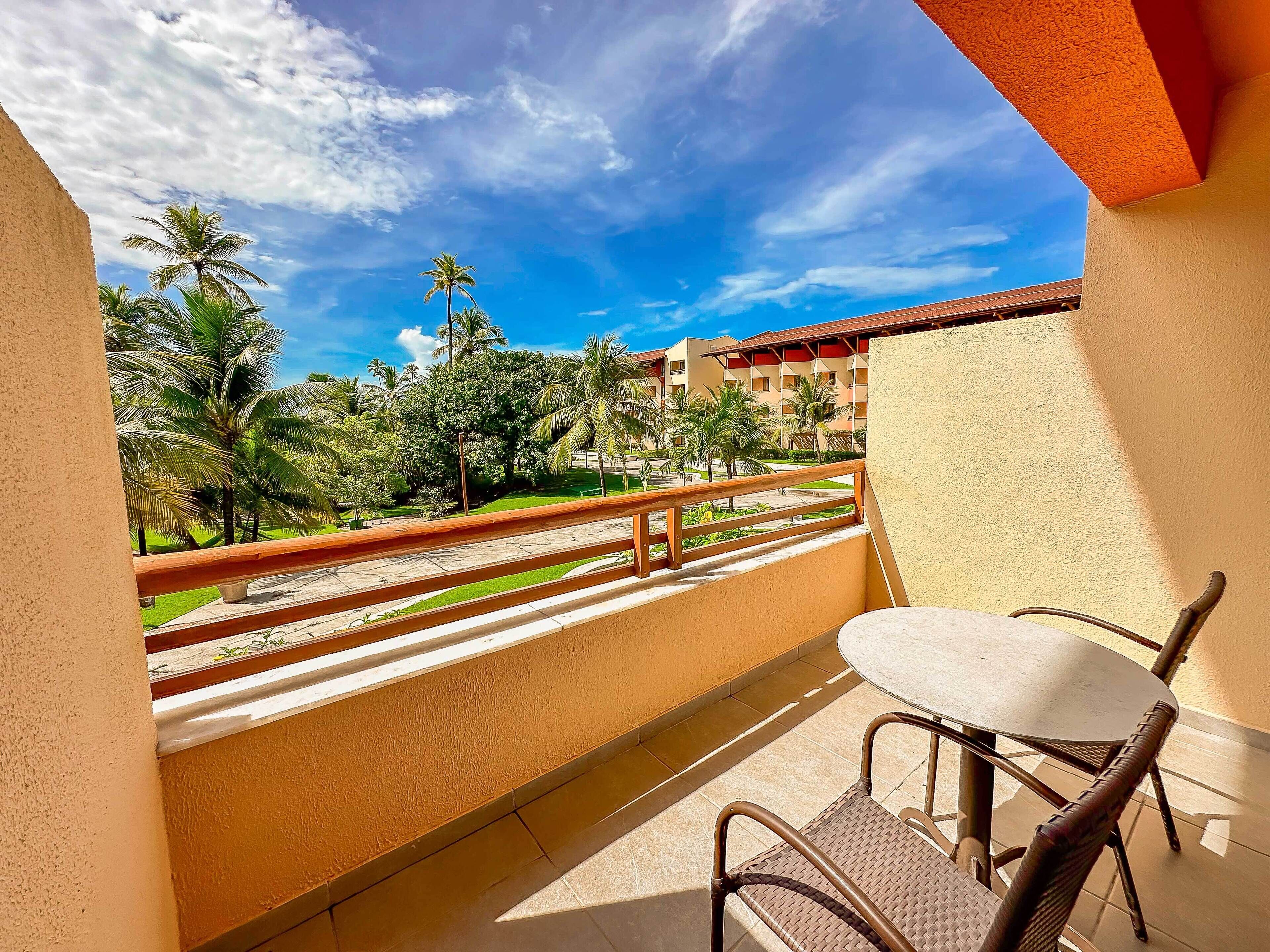A balcony with a view of a hotel complex, a table, and chairs.