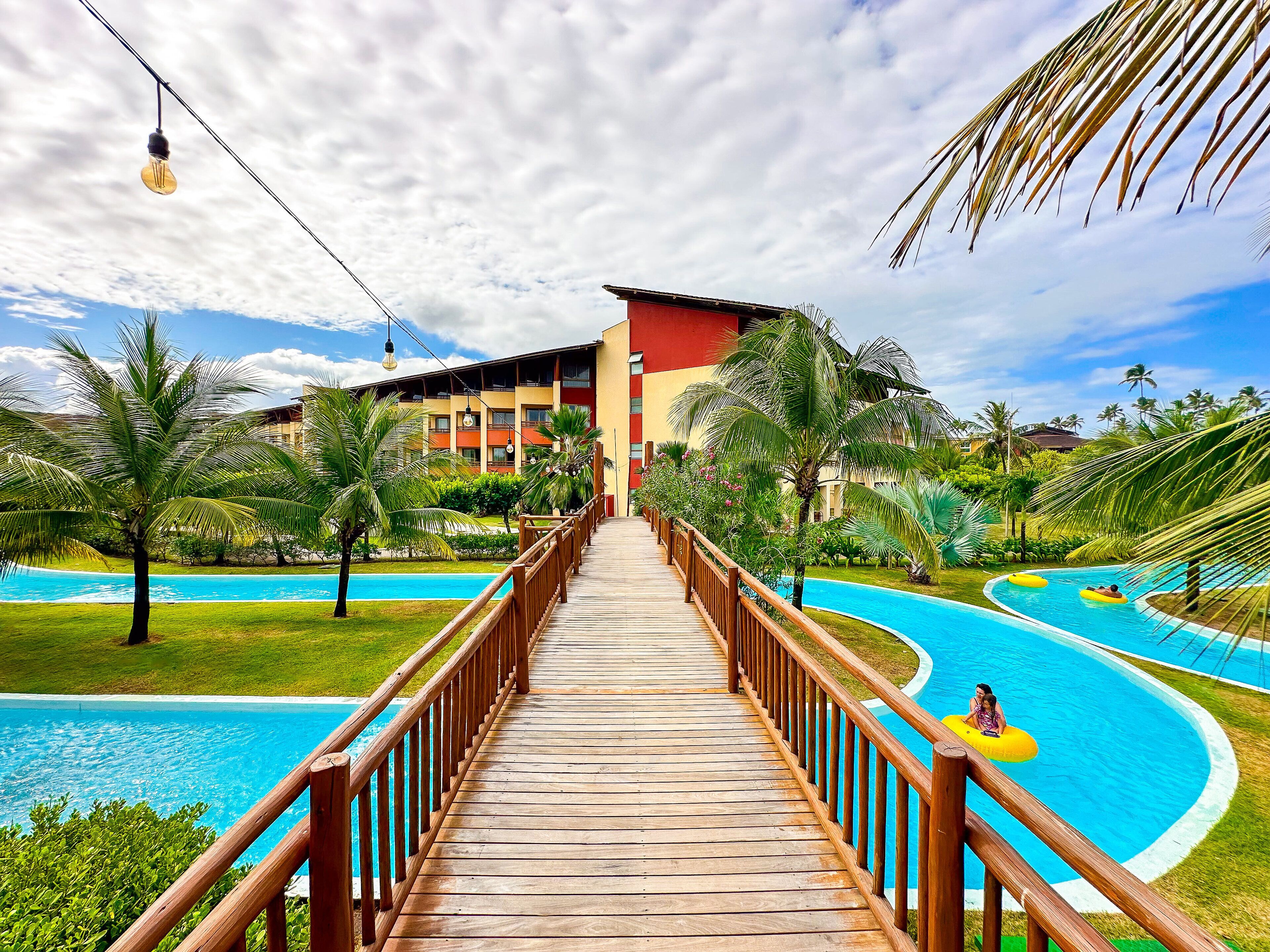 A wooden boardwalk leading to a pool area with a building in the background.