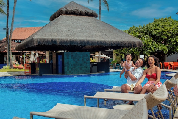 Una piscina con sillas de descanso, una estructura de techo de paja y un entorno tropical.
