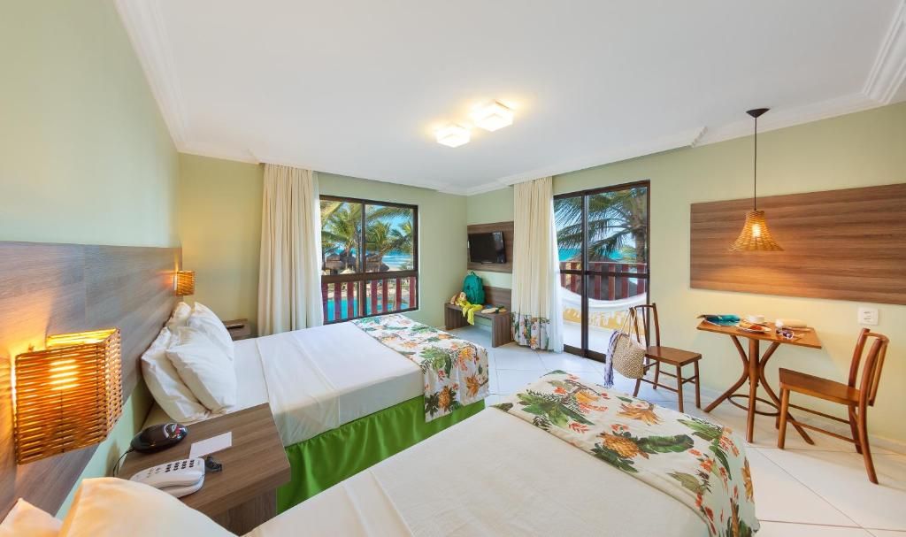 A hotel room with two beds, a desk, a chair, a TV, and a balcony with a view.