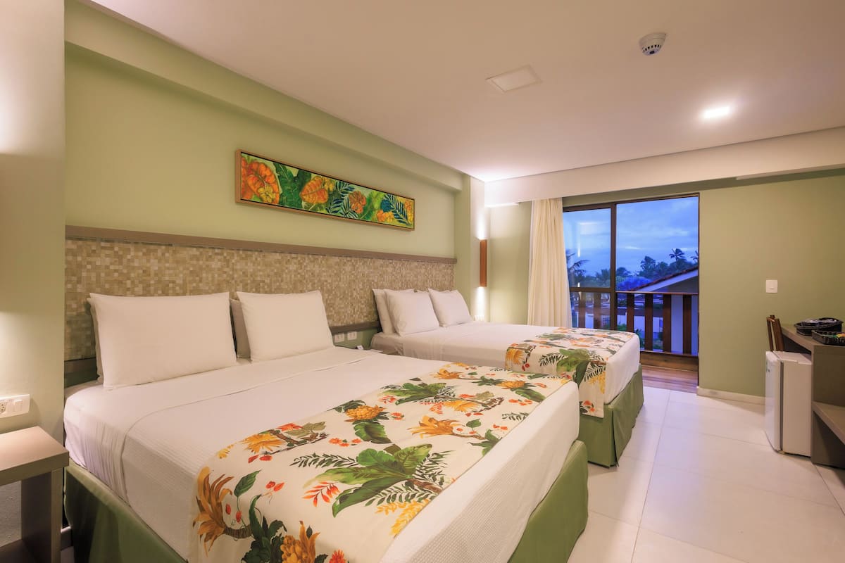 Habitació d'hotel amb dos llits, un balcó i vistes, i una cuineta petita.