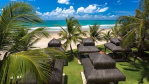 Un resort frente a la playa con sillones de techo de paja y palmeras, con vistas a un océano azul cristalino.