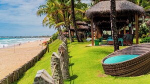 Un complejo turístico frente a la playa con cabañas de techo de paja, césped y una piscina.