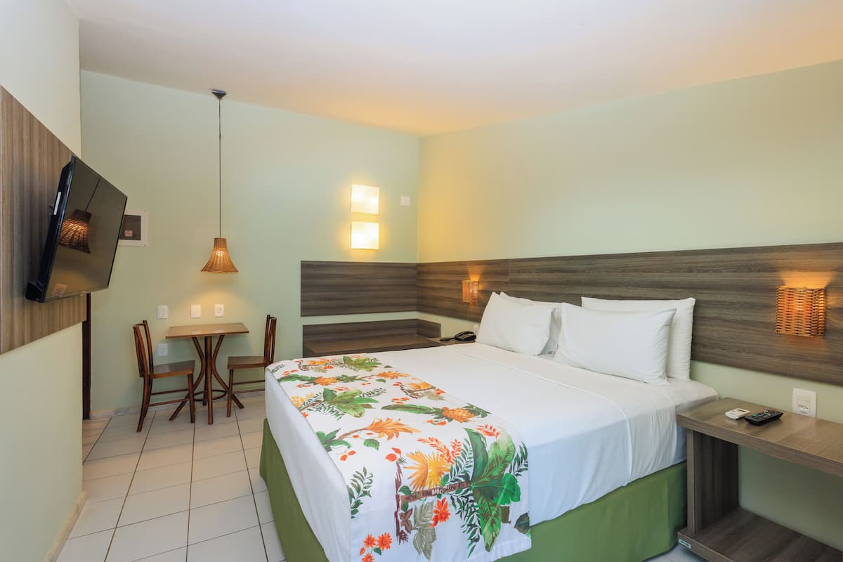 Habitació d'hotel amb llit, taulella de nit, cadira, taula petita i televisió penjada a la paret.