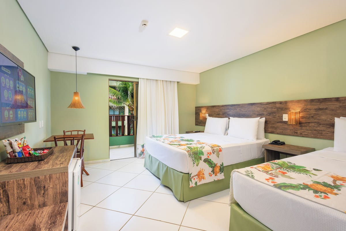 Habitació d'hotel amb dos llits, una taula de treball i una cadira. Hi ha una finestra amb cortines, un panell de fusta al capçal i un televisor fixat a la paret.