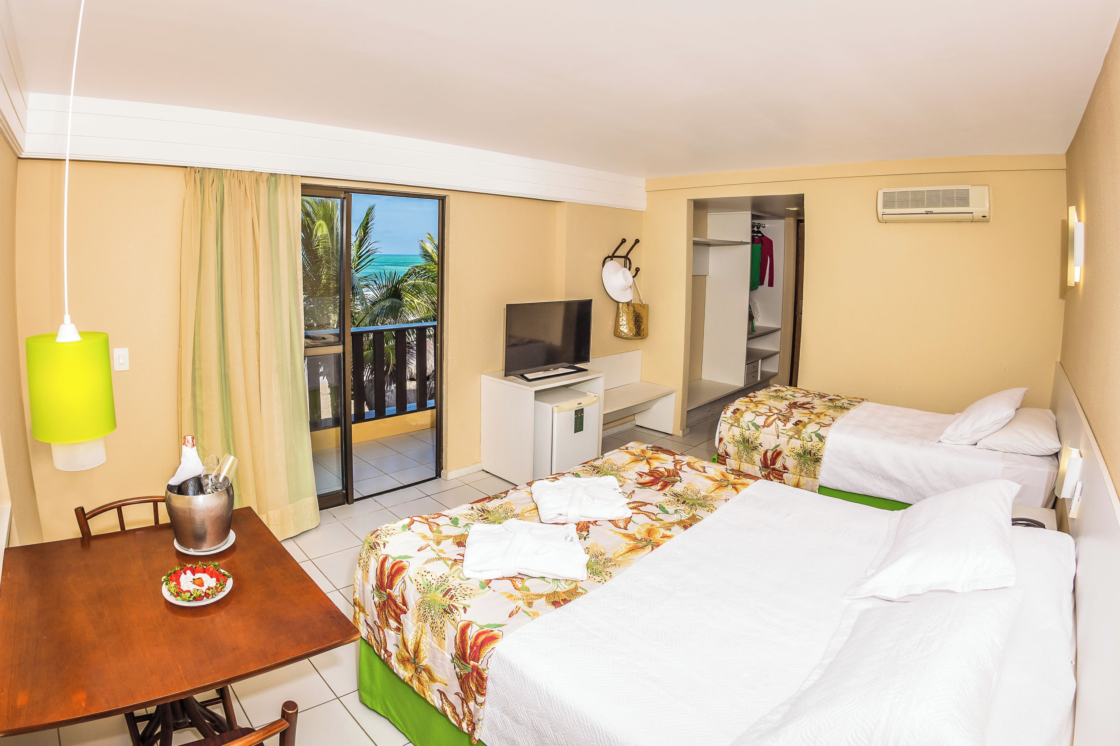 A hotel room with two beds, a dining table, a TV, and a balcony with a view.