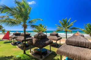 Un resort frente al mar con sombrillas de paja, palmeras y vistas al océano.