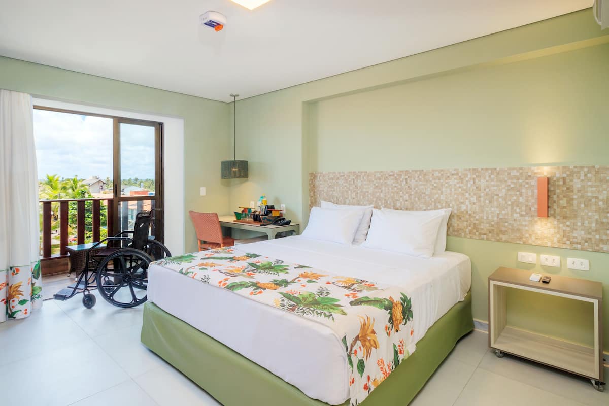 Habitació d'hotel amb llit, escriptori, cadira de rodes i balcó amb vistes.
