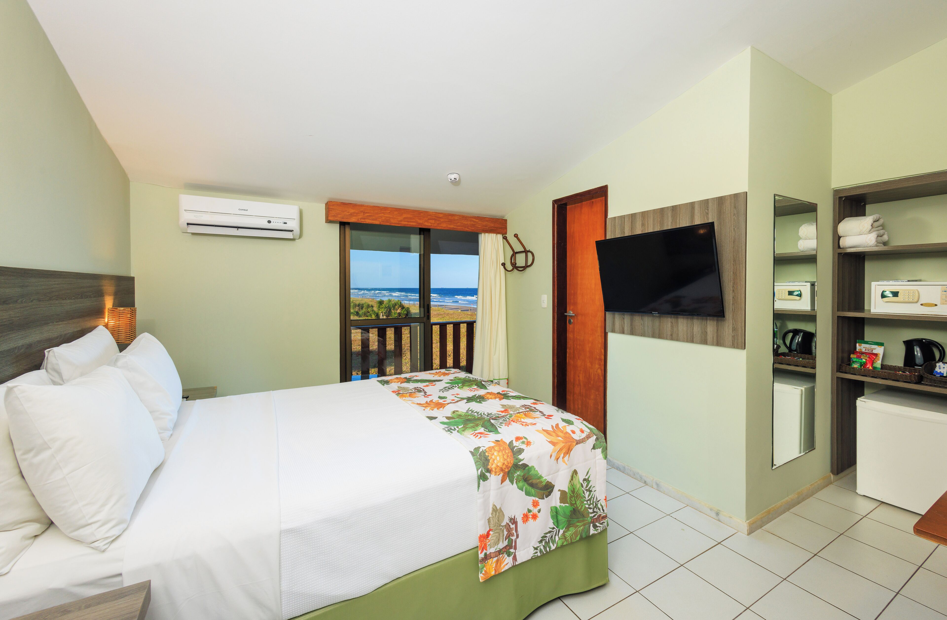 Een hotelkamer met een bed, een televisie, een kleine keuken en uitzicht op de oceaan.