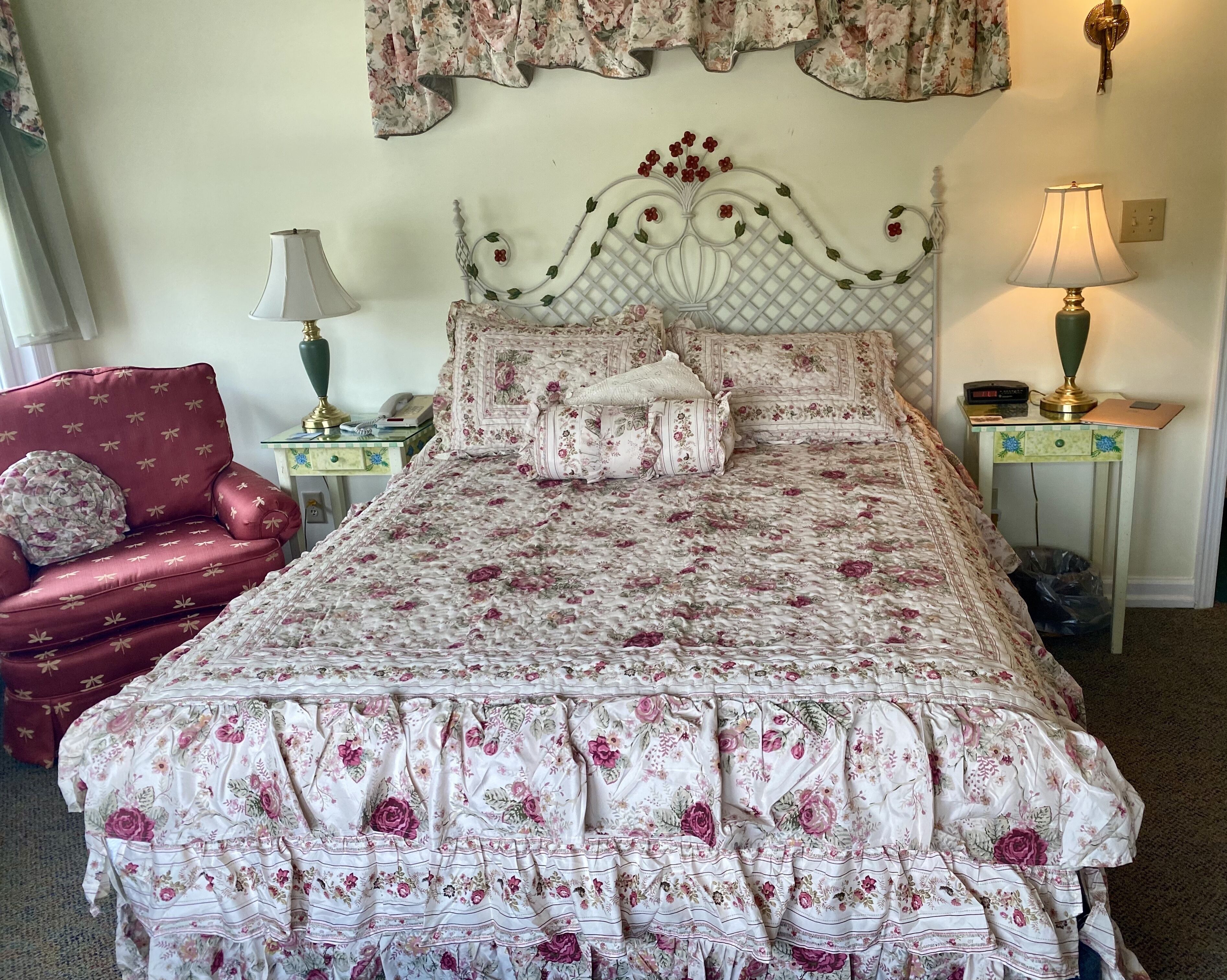 A neatly made bed with floral bedding, a red armchair, two bedside tables with lamps, and a decorative wall hanging.