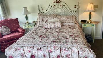 A neatly made bed with floral bedding, a red armchair, two bedside tables with lamps, and a decorative wall hanging.