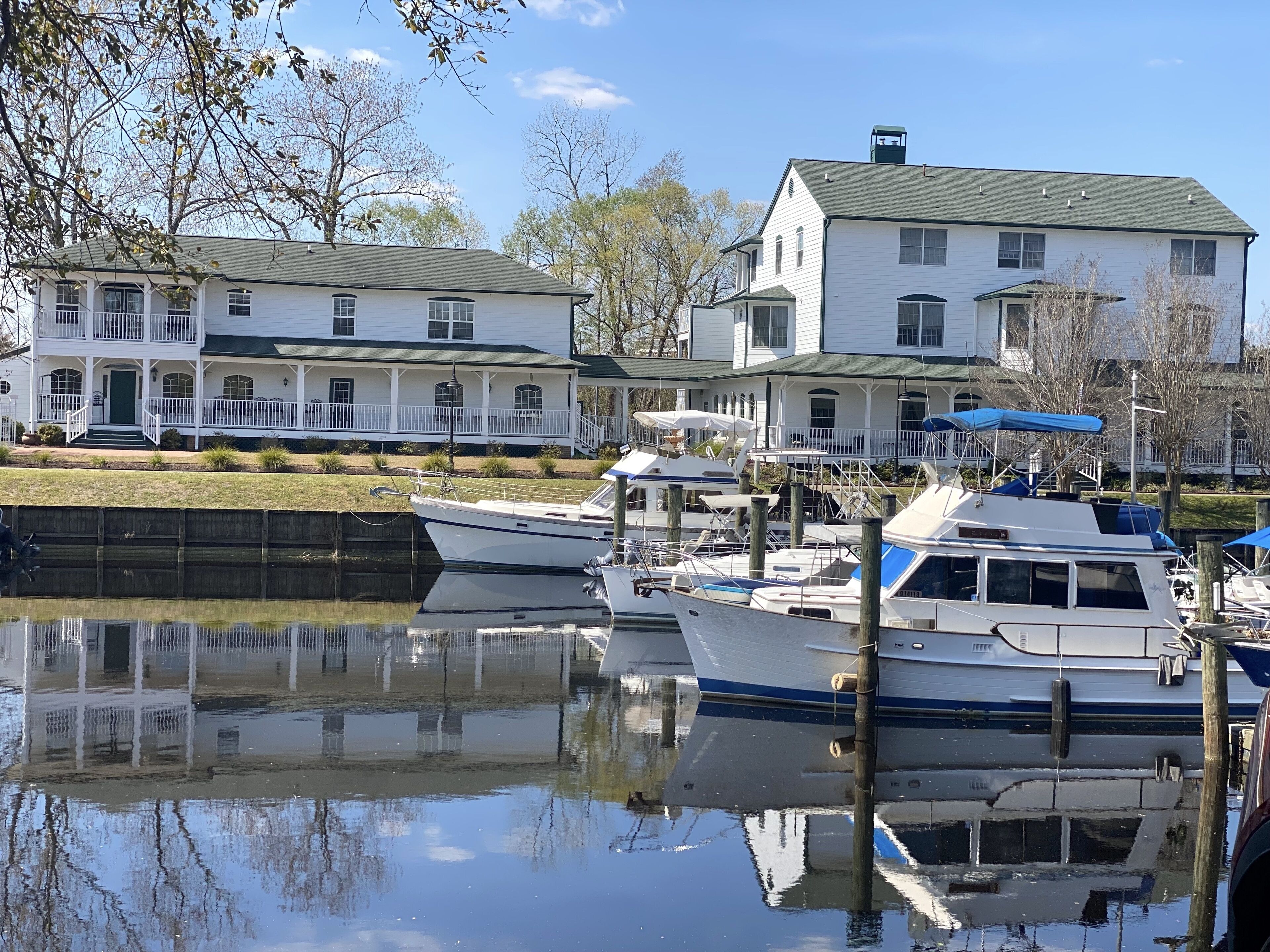 Un port de plaisance avec des bateaux amarrés, une maison blanche avec un toit vert et un ciel dégagé.