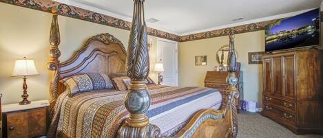 A four-poster bed with ornate headboard and footboard, a television on the wall, and a wooden dresser with drawers.