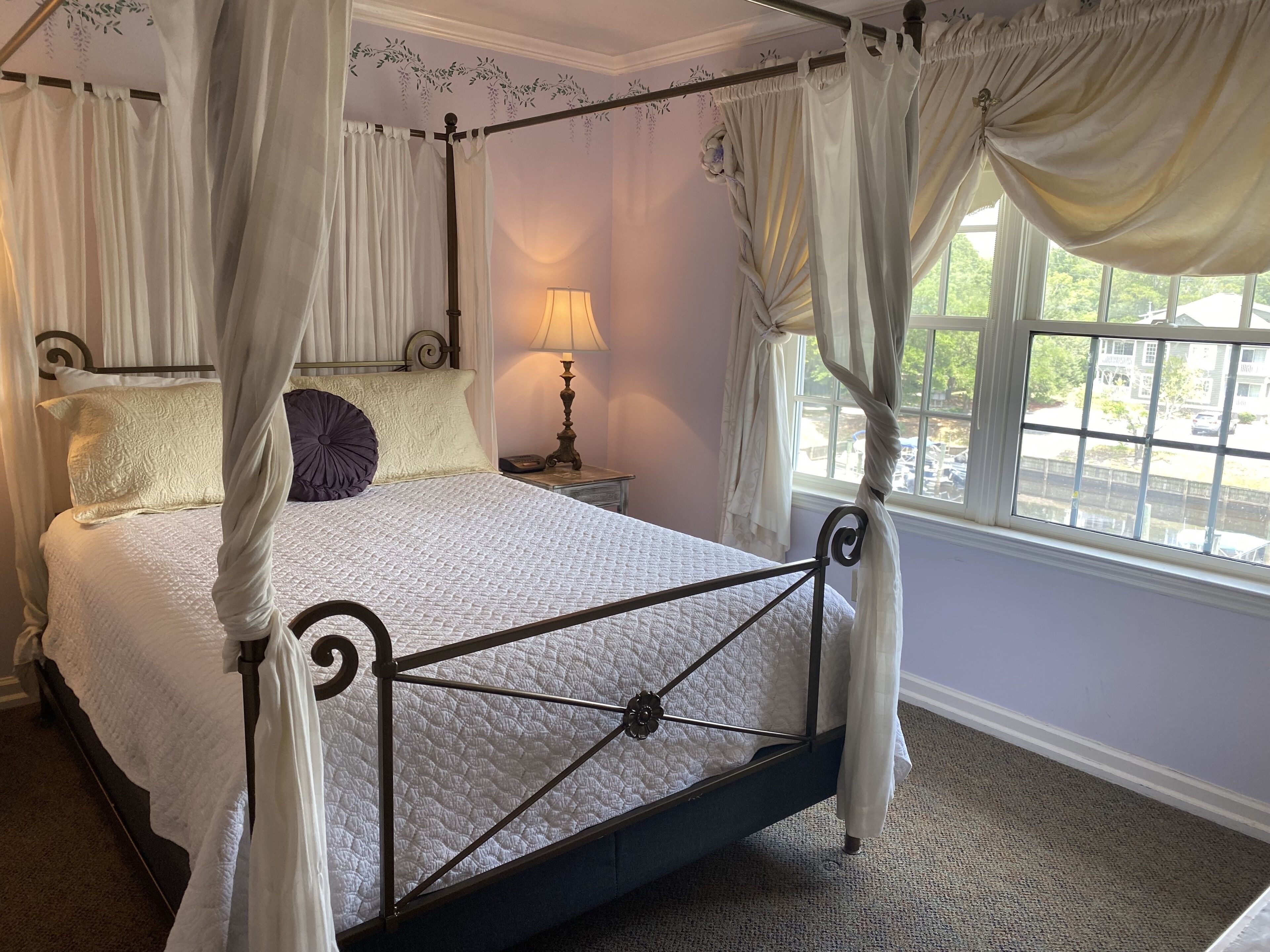 Una cama con dosel, una lámpara de noche y vistas al exterior a través de una ventana.