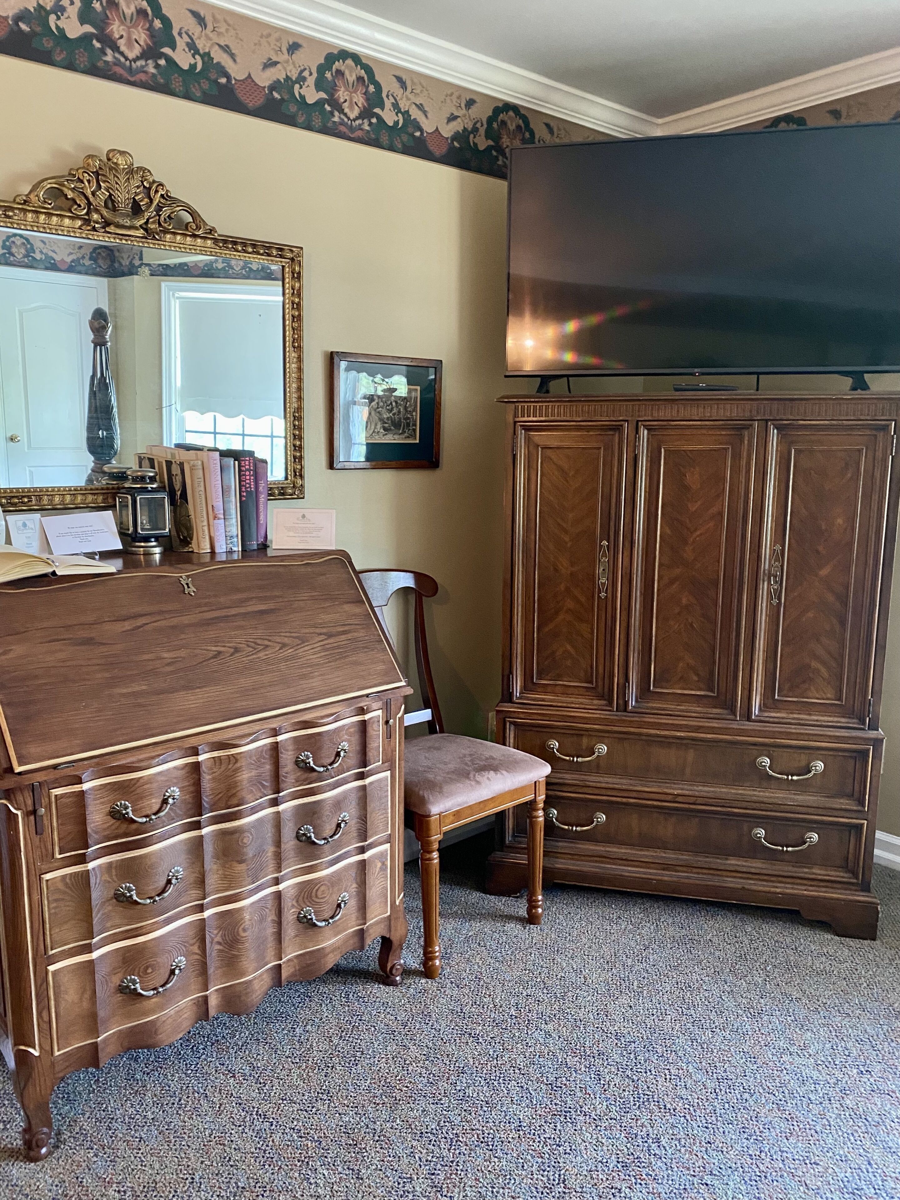 Une pièce comprenant une grande commode en bois, une chaise assortie, un miroir et un téléviseur.