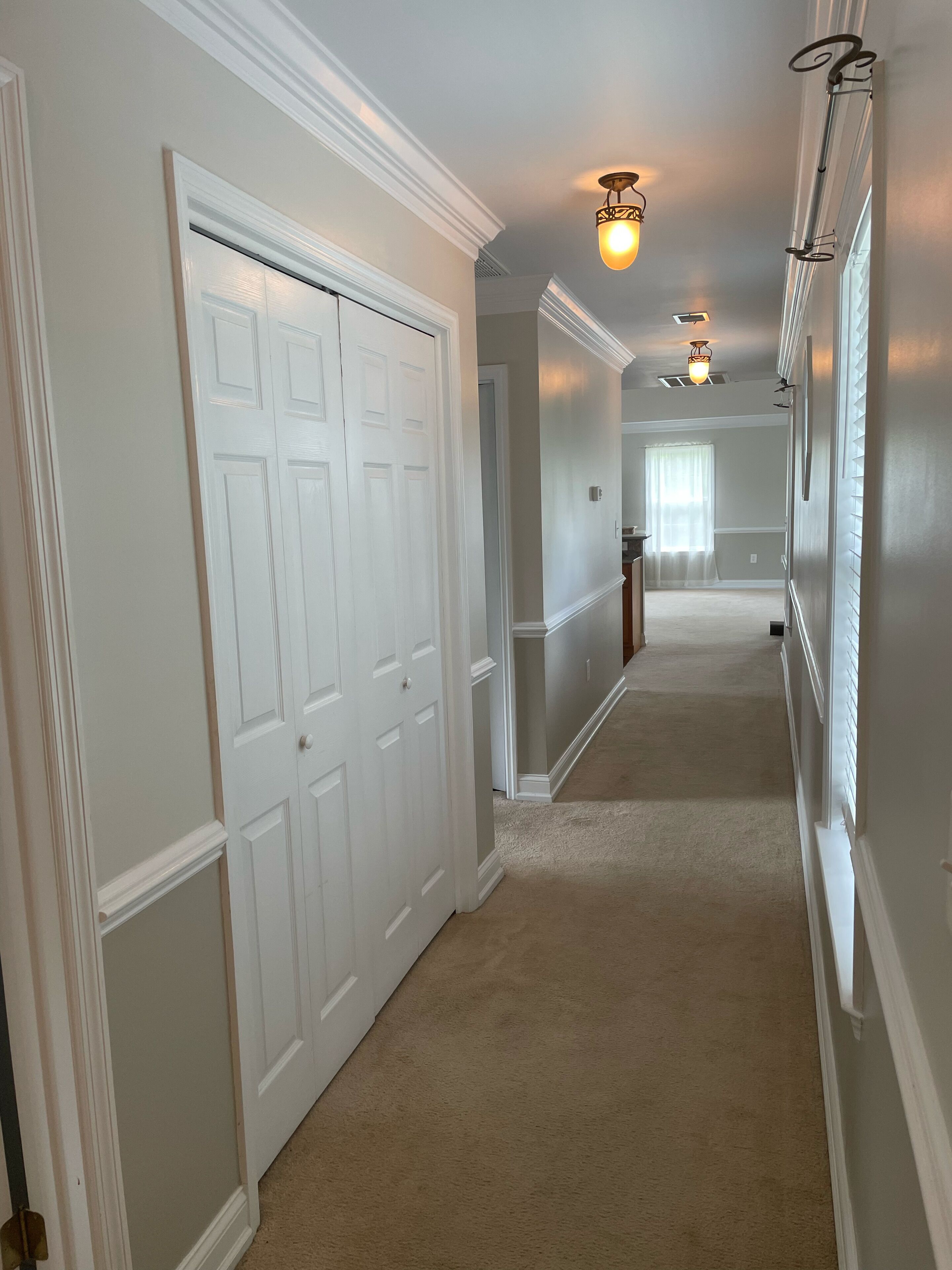 A hallway with white doors, beige carpet, and wall-mounted lighting fixtures.