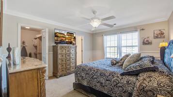 A bedroom with a bed, dresser, television, and a ceiling fan.
