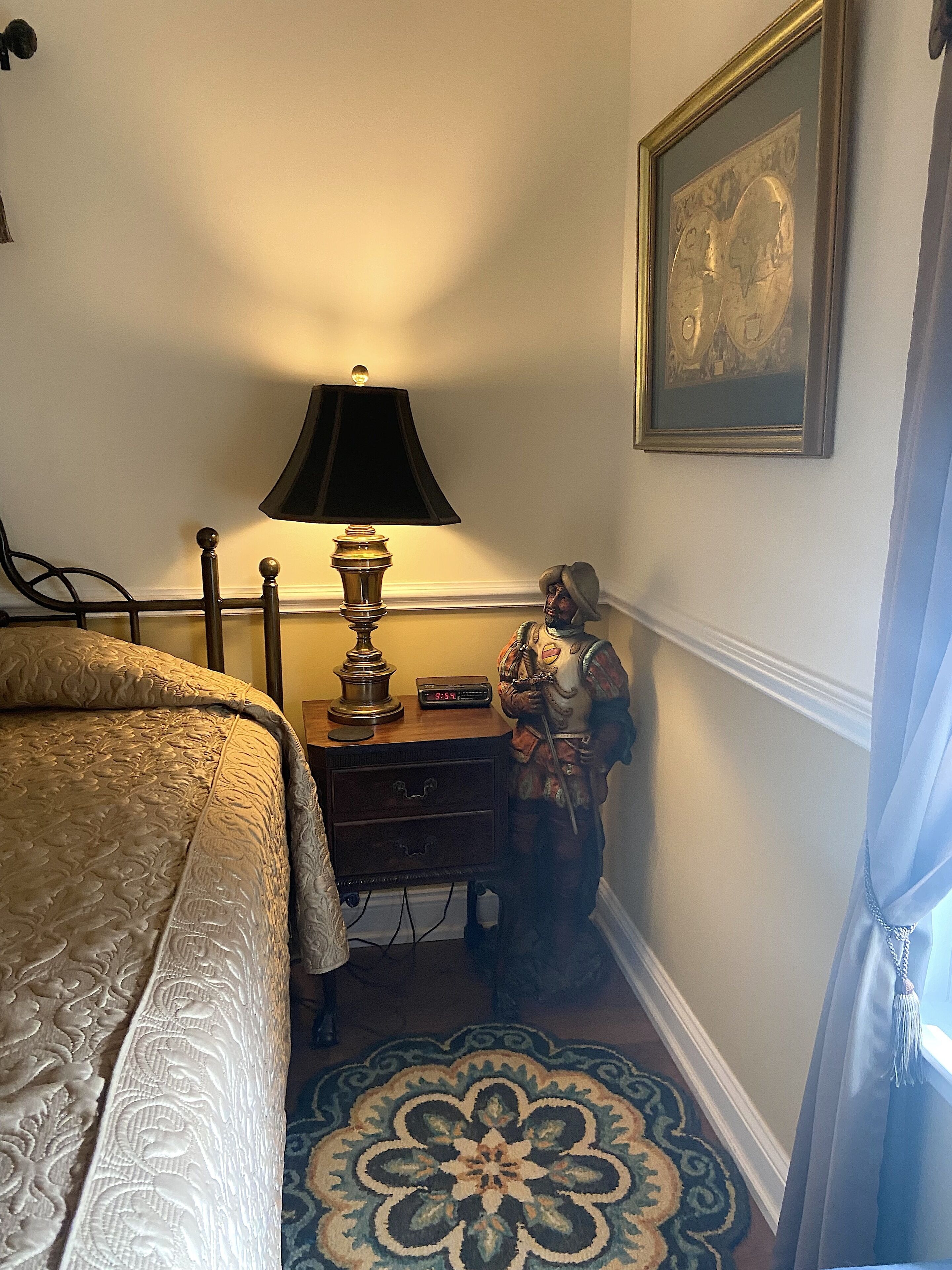 A bedroom with a bed, a nightstand, a lamp, a clock, a decorative statue, and a framed picture on the wall.