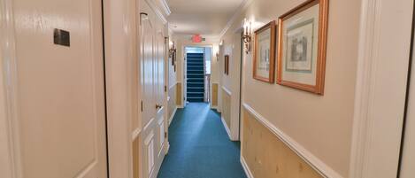 A hallway with cream-colored walls, a blue carpet, and framed pictures on the right.