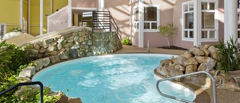 A pool area with a stone wall, metal railings, and a staircase leading to a building with large windows.