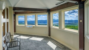 A room with large windows offering a view of a lake and mountains. There is a bench and a sign on the windowsill. - Steele Hill Resorts (Sanbornton)