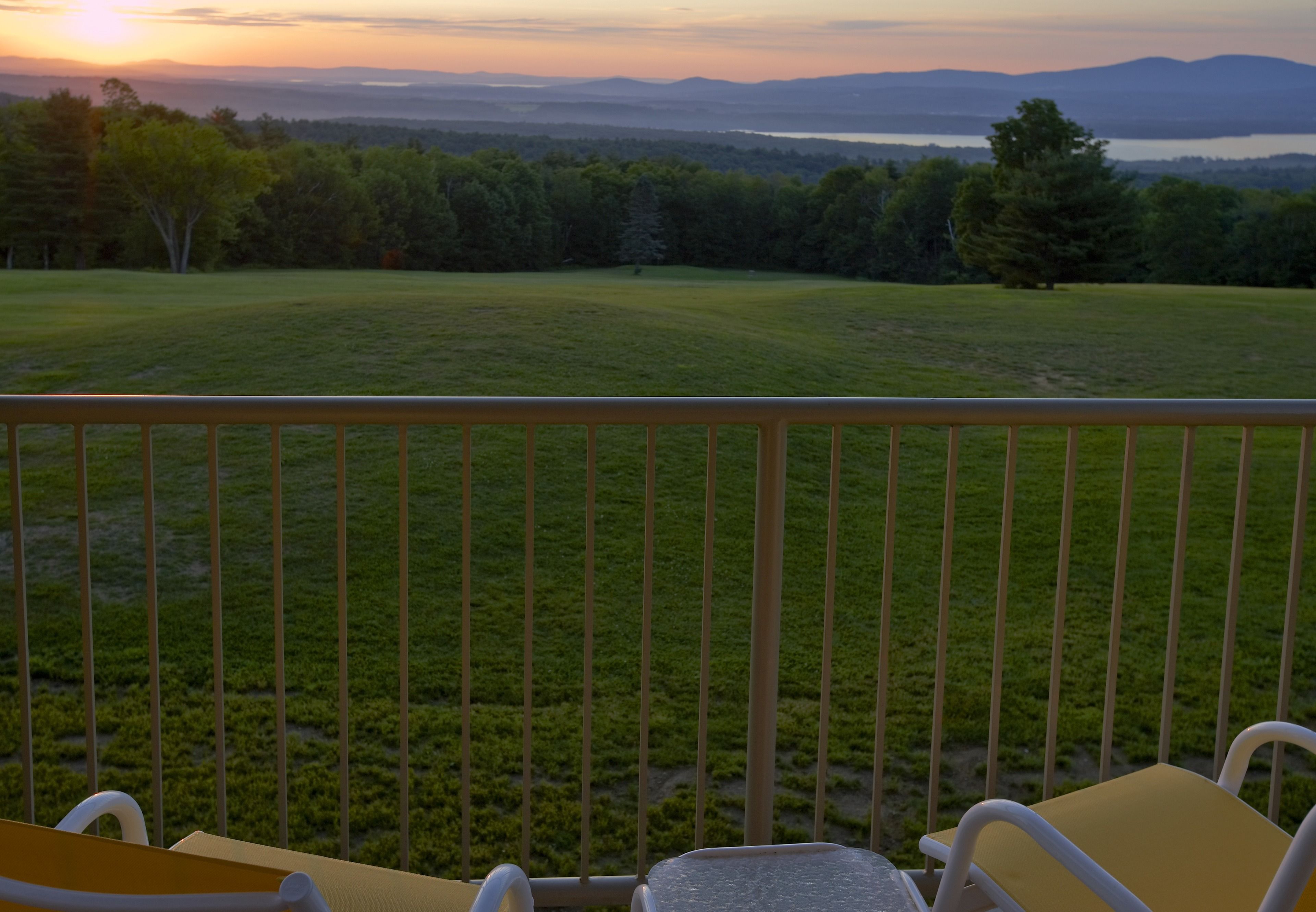 A balcony with a view of a grassy field and distant mountains.