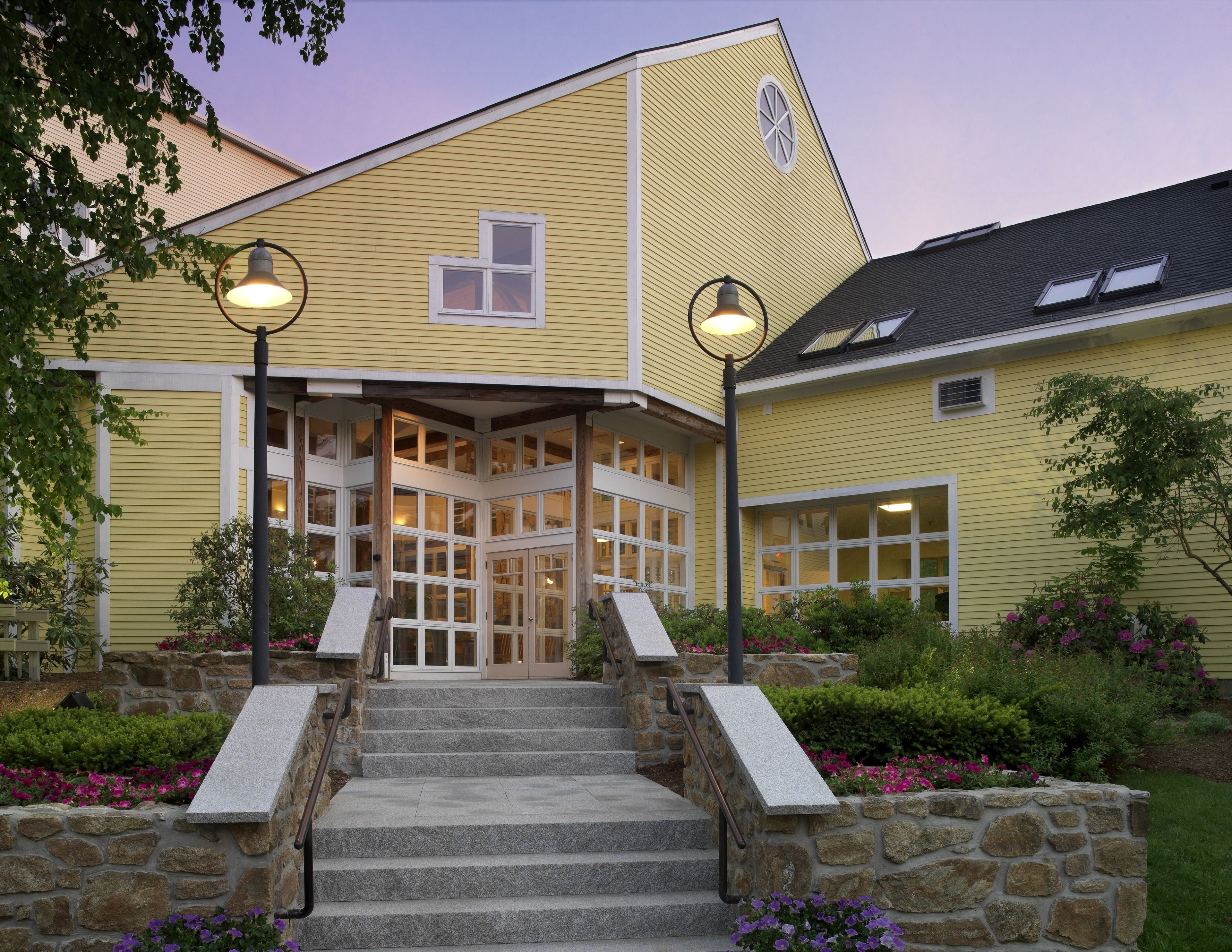 A yellow building with a corner entrance, stone steps, and a stone wall.