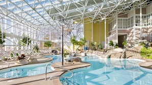 An indoor swimming pool with a glass ceiling, surrounded by lounge chairs and potted plants. - Steele Hill Resorts (Sanbornton)