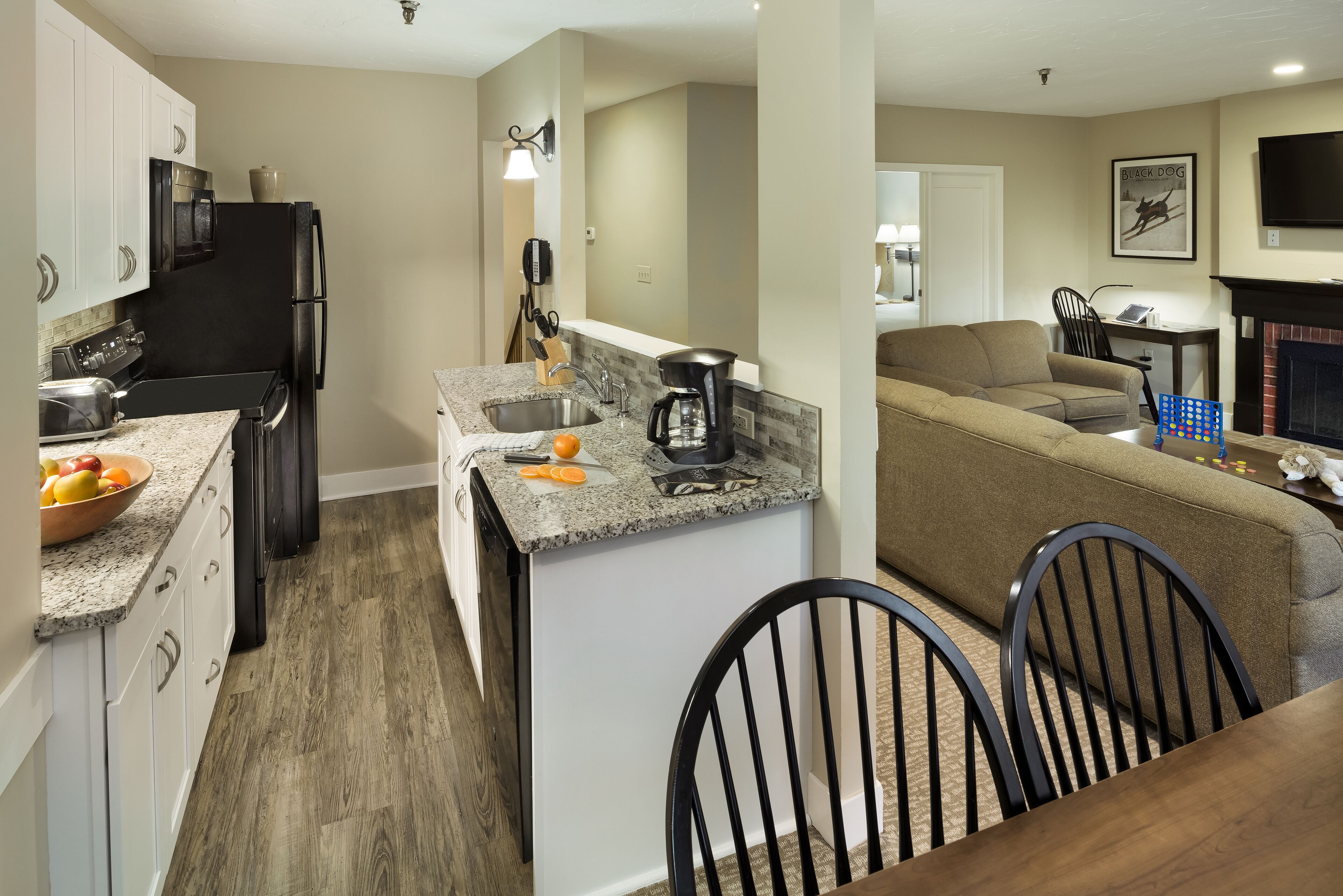 A modern kitchen with a built-in oven, microwave, and refrigerator. There is a dining area with a table and chairs, and a living room with a sofa and a fireplace.