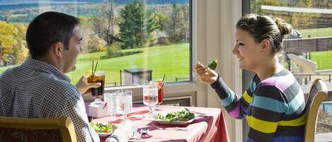 A dining table with a red tablecloth, a plate of salad, and drinks.