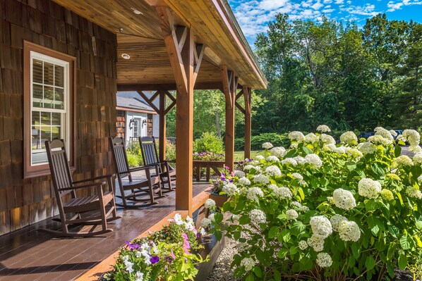 A wooden porch with rocking chairs and a garden with hydrangeas.