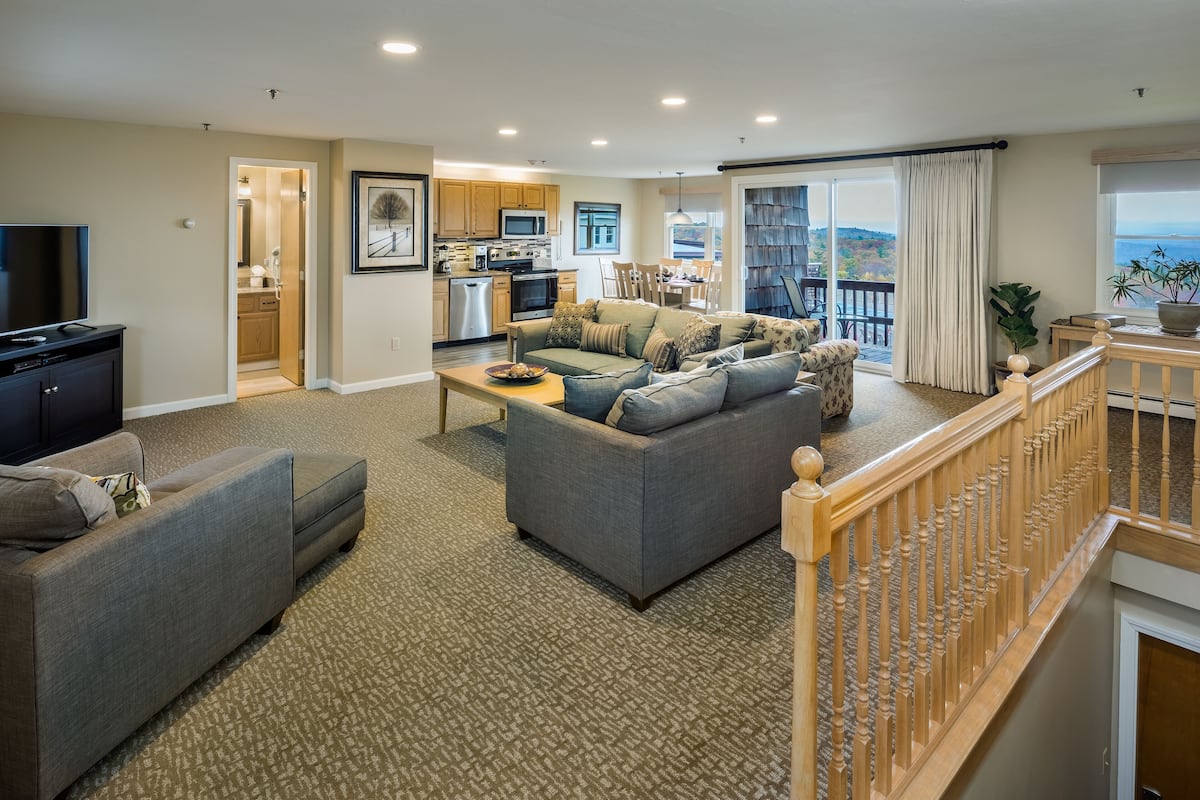 A spacious living area with a gray sofa, a television, and a kitchen in the background.