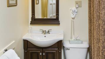Un baño con un lavamanos blanco, armarios de madera oscura, un inodoro blanco y un espejo con luces arriba.