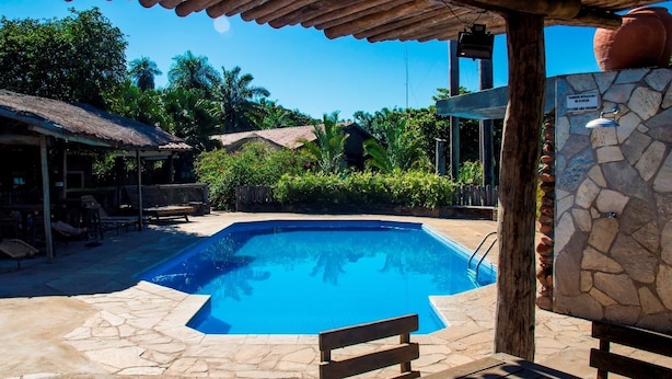 A swimming pool with stone tiles, wooden benches, and a pergola structure. - Pousada Aguape (Aquidauana)
