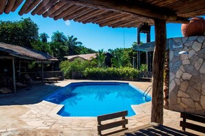 Piscina con baldosas de piedra, bancos de madera y una estructura de pérgola.