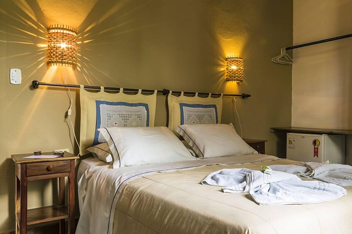 Una habitación de hotel con cama, dos mesitas de noche, una lámpara de pared y un refrigerador pequeño.