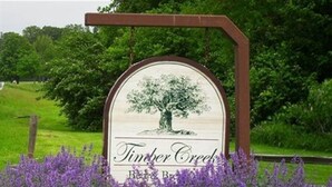 A sign with a tree and the text "Timber Creek Bed & Breakfast" surrounded by purple flowers. - Timber Creek Bed & Breakfast (Paxton)