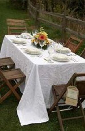 An outdoor dining table set with white tablecloths, plates, and a centerpiece. - Timber Creek Bed & Breakfast (Paxton)