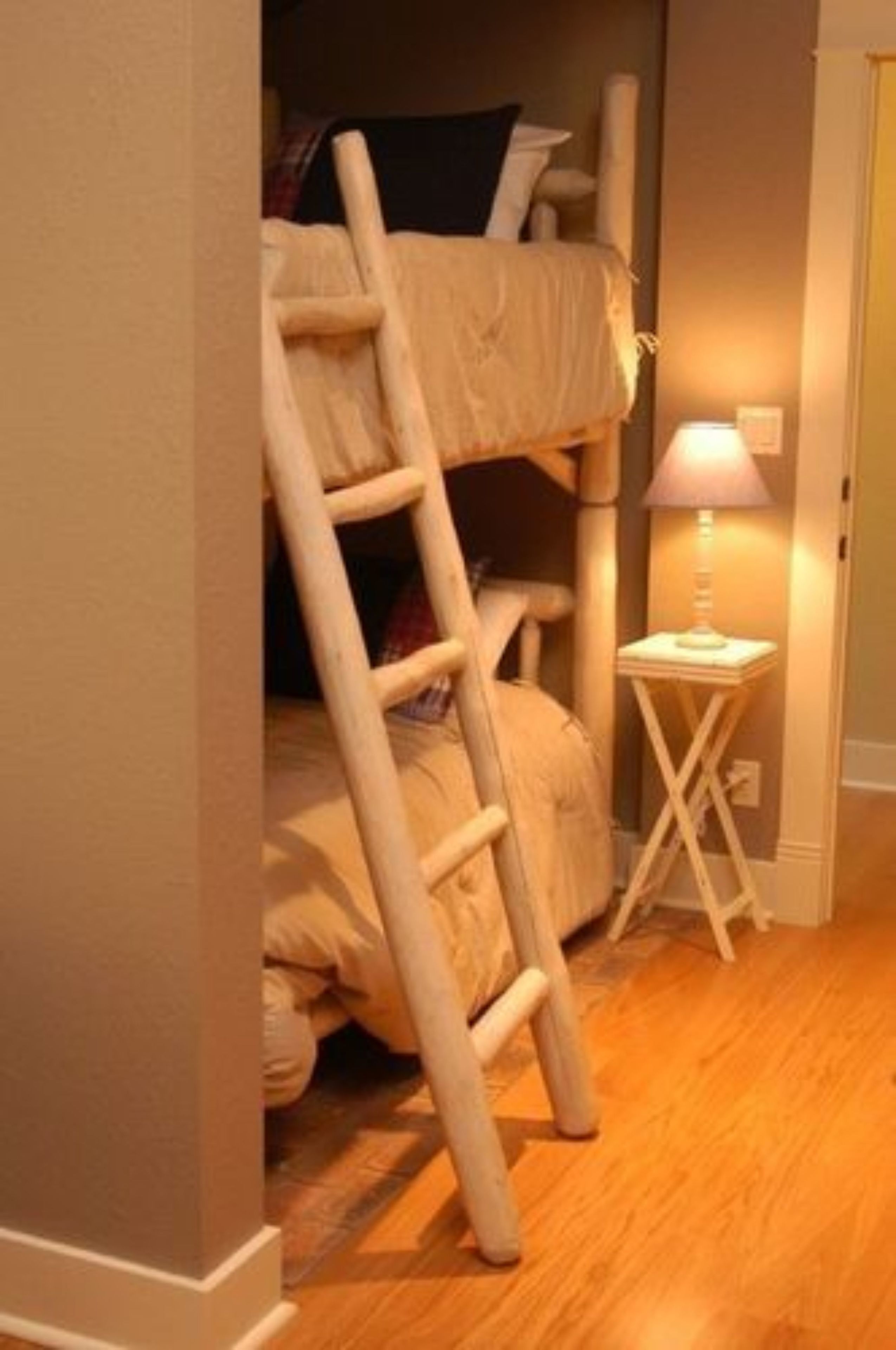 Una cama litera con una escalera, una mesita de noche con lámpara y suelo de madera.