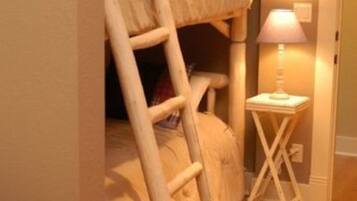 Una cama litera con una escalera, una mesita de noche con lámpara y suelo de madera.
