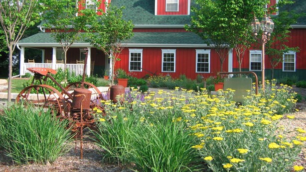 A red barn with a green roof, a porch, and a flower garden in front. - Timber Creek Bed & Breakfast (Paxton)