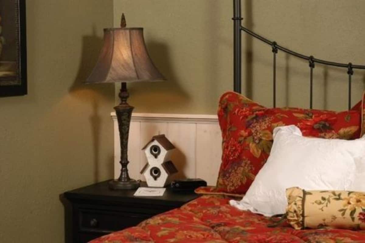 A bedroom with a bed, a nightstand, a lamp, and a wall-mounted shelf.