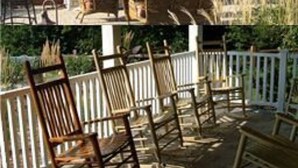 A stone fireplace with a chimney, surrounded by outdoor furniture and a white fence. - Timber Creek Bed & Breakfast (Paxton)
