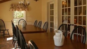 A dining room with a wooden table, black chairs, a chandelier, and a large window. - Timber Creek Bed & Breakfast (Paxton)
