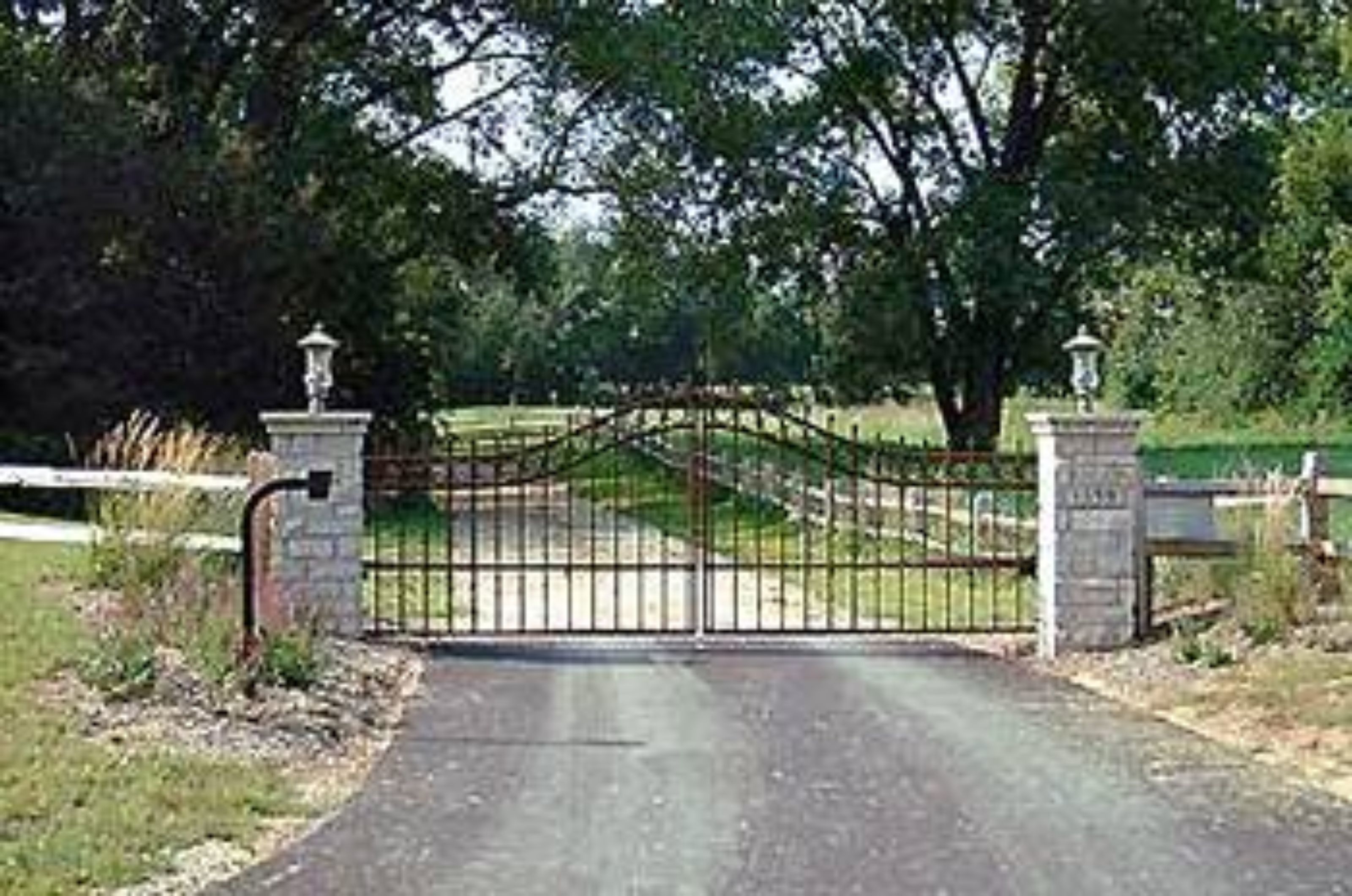 A gated entrance with a metal gate and stone pillars, surrounded by trees.