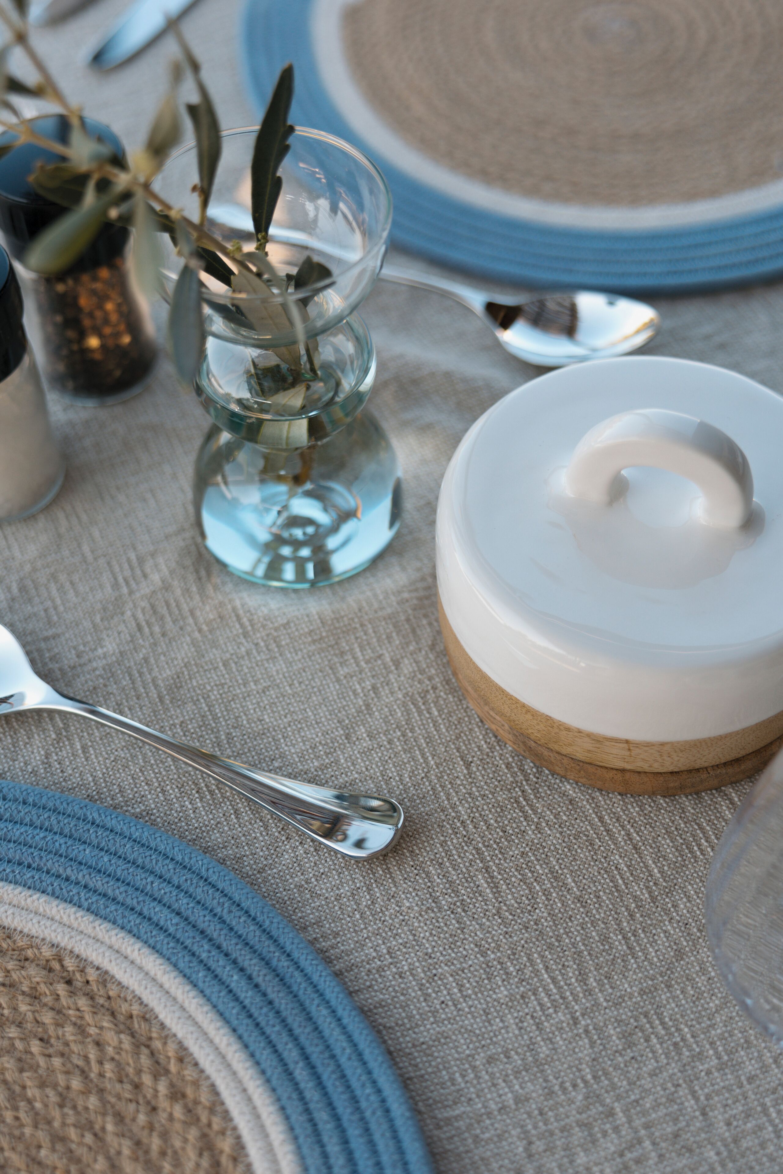 A table set with plates, a glass vase with a plant, and a white container with a lid.